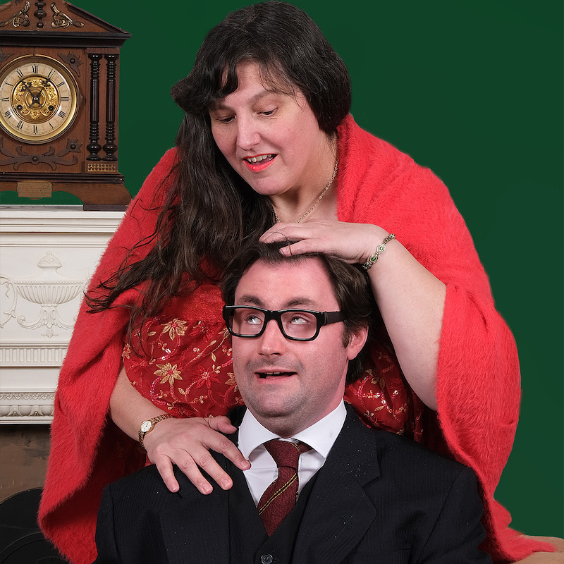 A woman in red pats the head of a man with glasses.