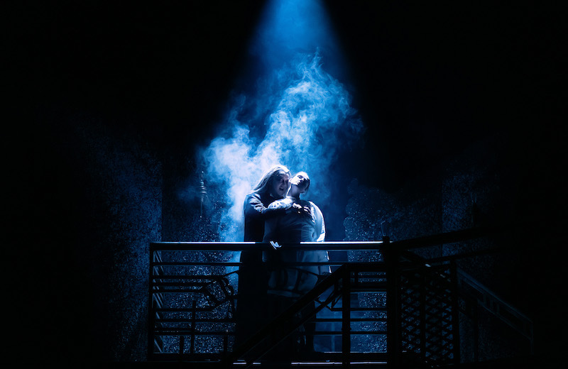 A dark stage with an eerie blue light illuminating Dracula as they prepare to feast on a lifeless Lucy.