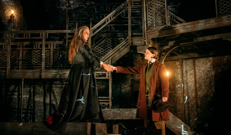 Jonathan and Dracula shake hands with their arms outstretched from their bodies as far as possible.