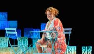 A woman with red curly hair in a red kimono sits on turquoise outdoor furniture.
